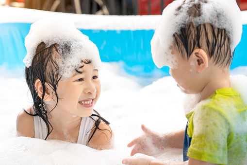 Cute Asian siblings having fun in the swimming pool. sister and brother playing with bubbles and swimming in the summer vacation pool. happy family holiday concept