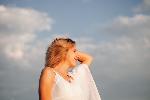 A beautiful woman against the background of clouds in profile. Romantic photo of a young happy smiling woman.