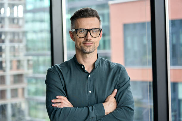 Smiling confident mature businessman looking at camera standing in office. Smiling confident mature businessman looking at camera standing in office. Elegant stylish corporate leader successful ceo executive manager wearing glasses posing for headshot business portrait. architect office stock pictures, royalty-free photos & images