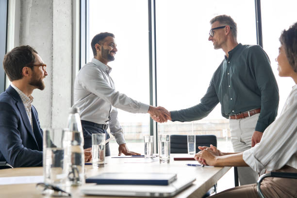istock Two happy diverse professional businessmen shaking hands at group board meeting. 1331101158