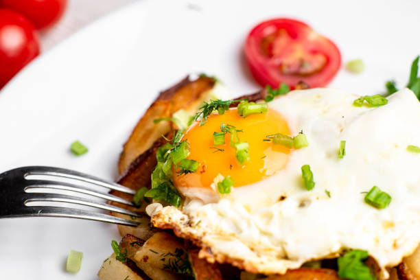 istock Fried potatoes with egg with liquid flowing yolk, herbs and tomatoes on a white plate. 1331102063