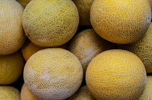 A retail display of yellow Canary melons are photographed from a high angle view as a background image