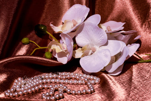 istock Pearl beads and white orchids. Composition on a satin shiny brown background. 1331107189