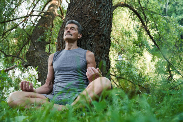 istock Man keeping eyes closed while sitting in yoga position at the forest 1331109685