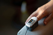 close up asian chinese mid adult woman's finger attached with oximeter measuring oxygen saturation in blood and heartbeat rate at home COVID-19 health technology