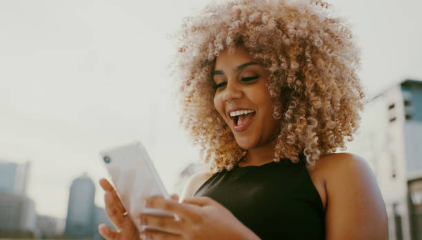 Shot of an attractive young woman standing alone and looking surprised while using her cellphone in the city