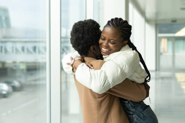 Couple reunion in airport: african female met hug boyfriend arriving after vacation or trip abroad Couple reunion in airport: portrait of happy african american female met hug boyfriend arriving from vacation trip abroad. Lovers after long separation due to coronavirus epidemic meet at end of covid airport hug stock pictures, royalty-free photos & images