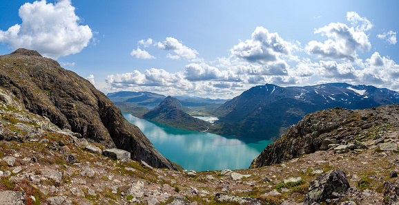 View from the cliff from Besseggen Ridge in Jotunheimen National Park, Norway. Panoramic views of the breathtaking green waters of Gjende Lake under blue skies.