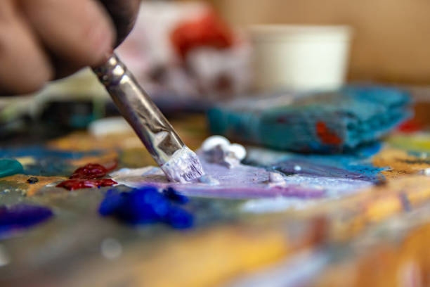 closeup of hand mixing paint on palette at workshop - kunst stockfoto's en -beelden
