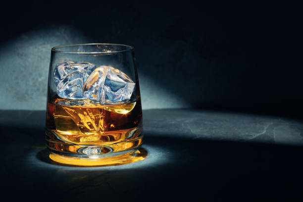 At the end of a hard day Late night glass of malt whisky with ice on a slate table with moonlight through the window on the wall behind. Glass of Whiskey stock pictures, royalty-free photos & images