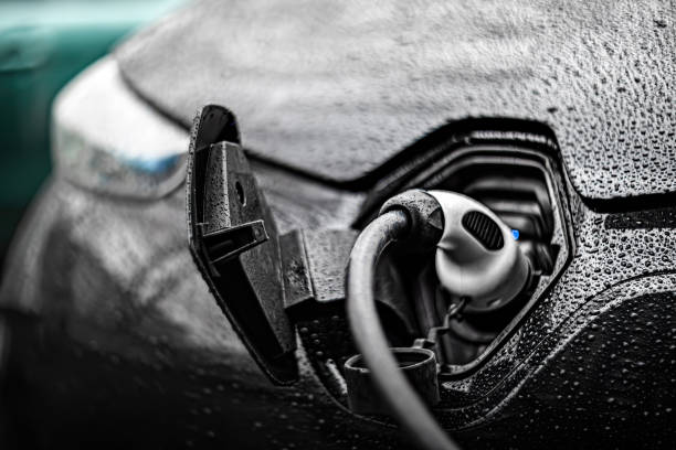 Black electric car (EV, electric vehicle) charging, rainy weather, beautiful artistic bokeh, soft focus. Saint-Petersburg, Russia, 21.04.2021