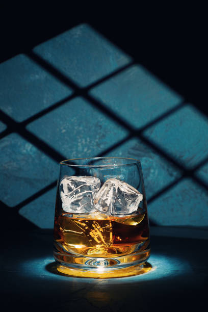 At the end of a hard day Late night glass of malt whisky with ice on a slate table with moonlight through the window on the wall behind. scotch whisky stock pictures, royalty-free photos & images
