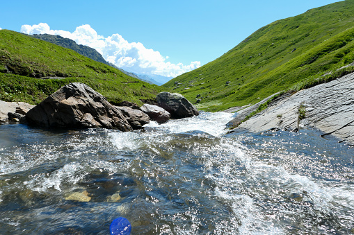 Water flowing of rapids between rock and pasture.