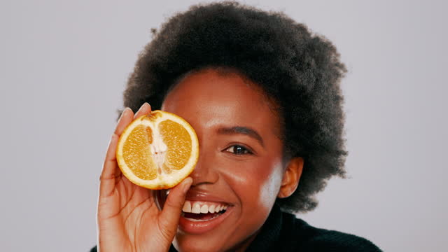 4k video footage of a young woman holding up a halved orange while posing against a grey background