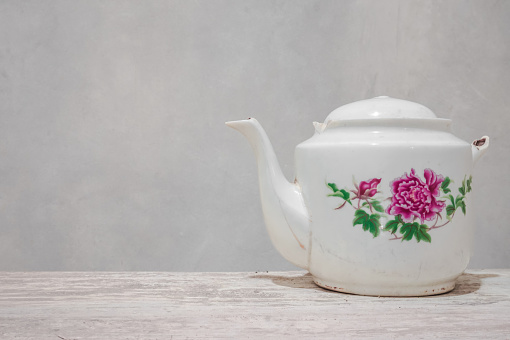 White ceramic teapot with pink flowers and green leaves.  ceramic teapot on a wooden table.  classic ceramic teapot
