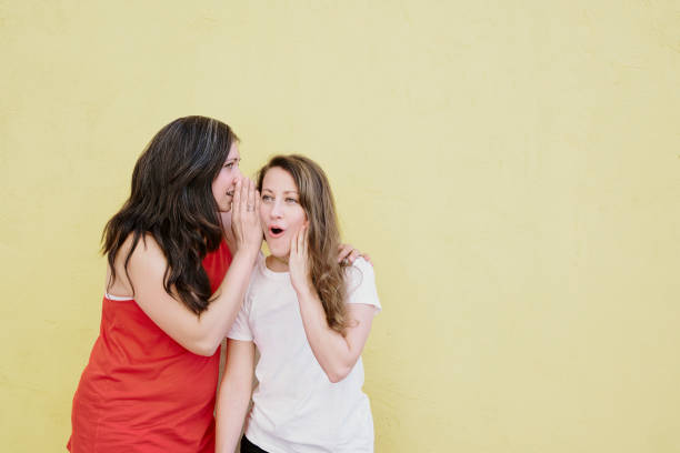 istock Two woman sharing secrets in the ear with an astonished face. 1331131041