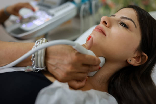 primo piano di una giovane donna che si fa esaminare il collo dal medico utilizzando lo scanner ad ultrasuoni presso la clinica moderna - thyroid gland foto e immagini stock