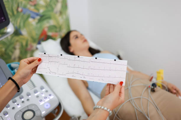 istock Young woman lying on bed with electrodes while doctor holding and analyzing printed electrocardiogram results 1331135251