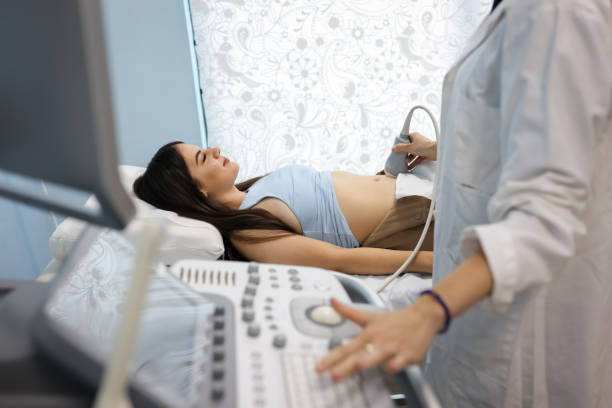 Doctor examining female abdomen with ultrasonography device Doctor examining abdomen of young female patient with ultrasound machine in hospital artificial insemination stock pictures, royalty-free photos & images
