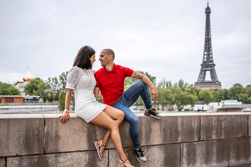 Photo of young couple having fun while looking at each other in Paris near Eiffel Tower.