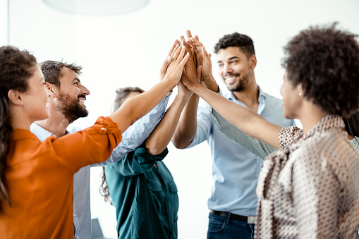 High-five for success! Diverse group of business colleagues giving each other high-five in a symbol of unity and smiling while working in the board room
