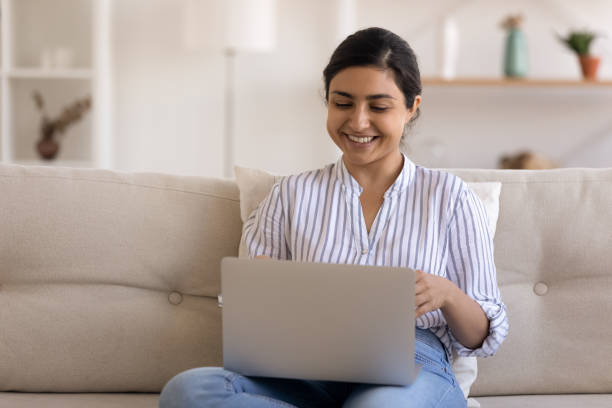 istock Smiling Indian woman using laptop, having fun, sitting on couch 1331150804