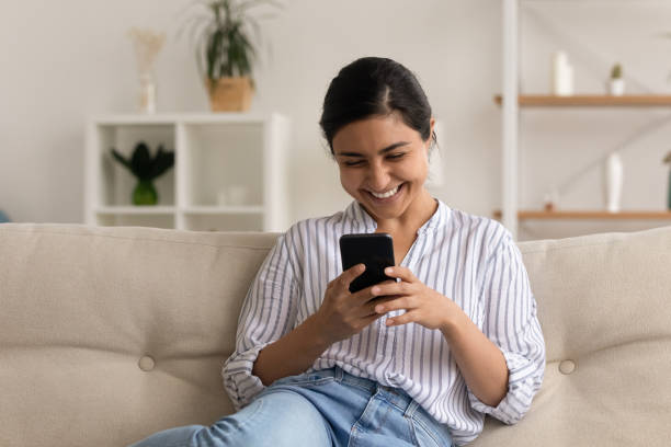 istock Excited Indian woman using smartphone, sitting on couch at home 1331150906