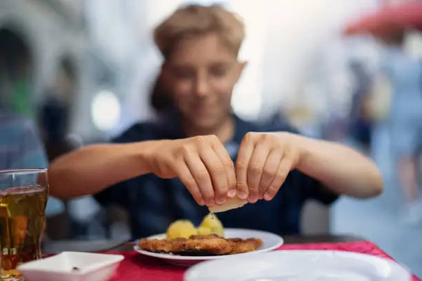 Teenage boy eating wiener schnitzel in a restaurant. The boy is squeezing lemon over the schnitzel.
Nikon D850