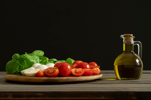 Olive oil bottle on black background with copy space. Mediterranean food.  Dressing fresh vegetables salad.