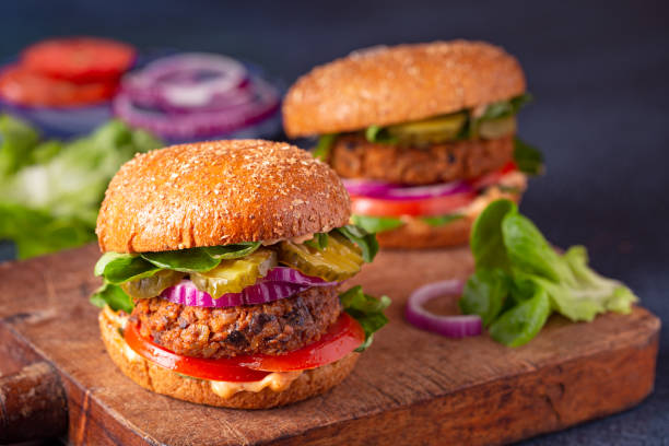 Two veggie burgers with ingredients on a wooden cutting board Homemade plant based burgers made from sweet potato, black beans and brown rice on a whole wheat brioche bun; copy space veggie burger stock pictures, royalty-free photos & images