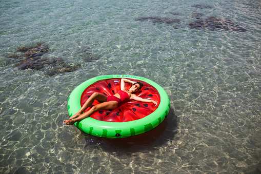 An attractive young woman is sunbathing on a big watermelon floatie at the seaside