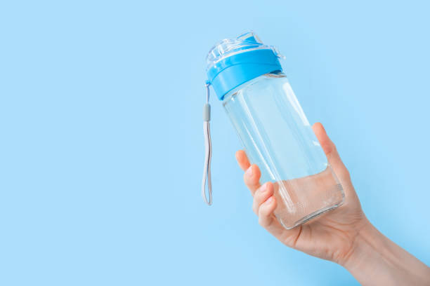 trinkwasserflasche für sport in weiblicher hand auf blauem rücken mit kopierraum. wiederverwendbare flasche. gesundes lifestyle- und fitnesskonzept - wasserflasche stock-fotos und bilder