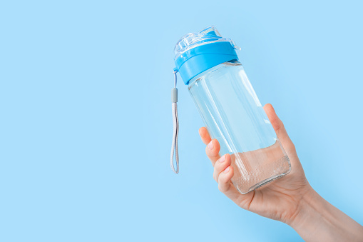 Botella de agua potable para deportes en mano femenina sobre backgraund azul con espacio de copia. Botella reutilizable. Concepto de estilo de vida saludable y fitness photo
