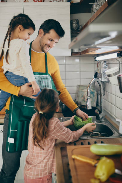 istock Happy father and daughters washing lettuce while preparing salad in the kitchen. 1331161438