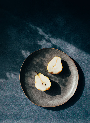 Fruit for breakfast: A plate with a halved pear ready to eat on a blue table