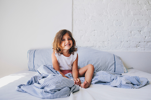 Smiling young girl waking up in the morning and looking at camera in the bedroom