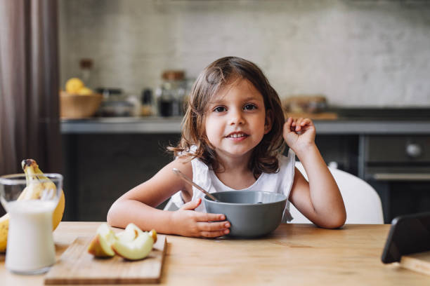 istock Cute Little Girl Looking at Camera While Eating Cereals for Breakfast at Home 1331173218