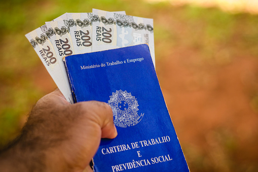 In this photo illustration the a man displays his Work and Social Security Card (Carteira de Trabalho e Previdencia Social) in Brazil with four bills of two hundred reais.