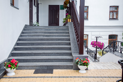 flowerpots with flowers at the staircase of the front porch with doors of the building faced with granite stone with wooden railings the exterior of the backyard architecture with bushes, nobody.