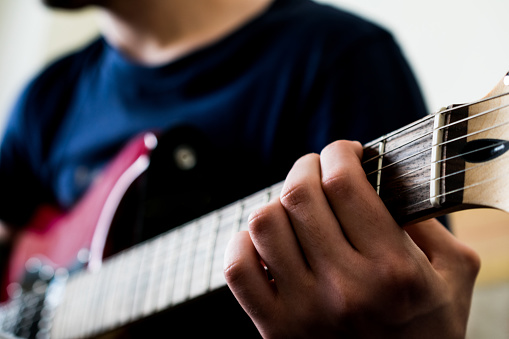 Bottom view of an unrecognizable man playing an electric guitar. Highly contrasted,view from the headstock of the guitar. The guitar is blurred, only the hand is in focus.