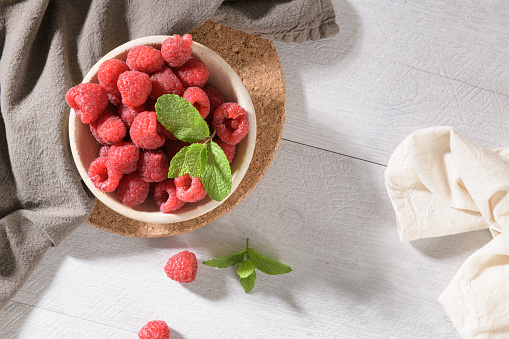 Ripe sweet raspberries in bowl on wooden table. Close up, top view.
