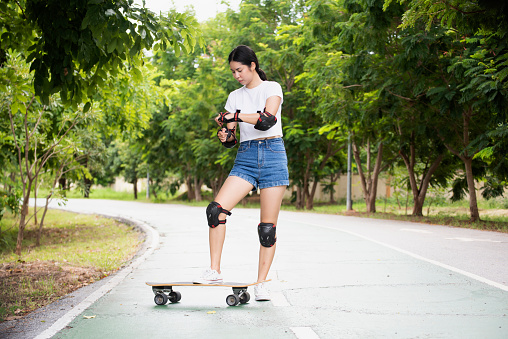 Woman surf skate board putting on elbow protector pads on her arm and wearing wrist guards and Safety.