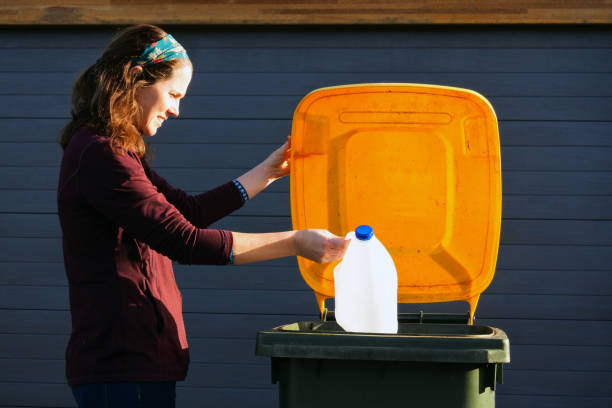 istock Woman puts a plastic milk bottle into a yellow recycling bin 1331199279