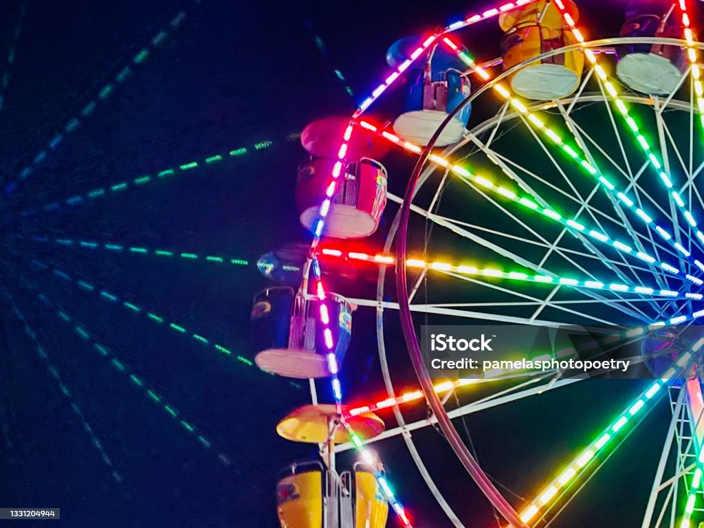 Vivid vibrant multicolored lights of Ferris Wheel at Lens reflection of bright colorful Ferris Wheel lighting, small town summer celebration. Minimalist style of lighted carnival ride, amusement park Ferris Wheel on summer evening. Recreational summertime fun. Ferris Wheel background. Traveling Carnival Stock Photo