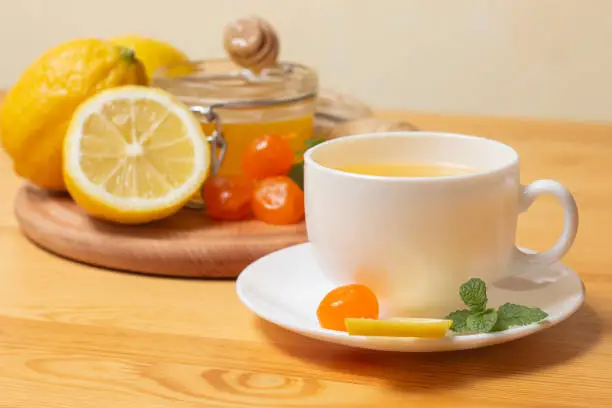 Ginger tea with mint and lemon. Healthy and hot drink. Liquid honey in honey-jar. White cup on wooden background. Selective focus. High quality photo