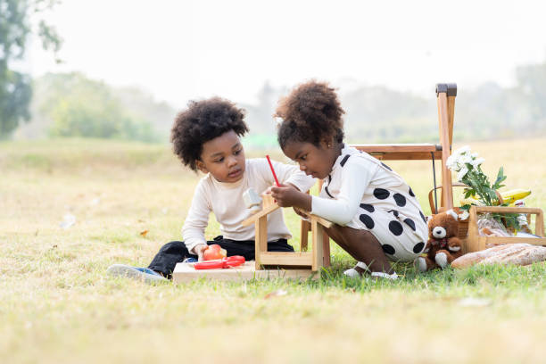 dos niños y niñas afroamericanos jugando al juguete juntos en el parque. los niños con el pelo rizado divirtiéndose juntos al aire libre. niños negros disfrutando de la calle - family grass toddler african descent fotografías e imágenes de stock