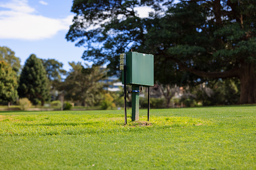 Green metal box on a stand with electrical outlets in a public park.