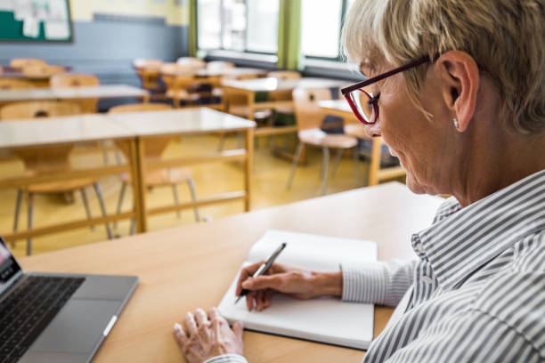 insegnante senior sorridente che prende appunti in classe. - grading teacher desk writing foto e immagini stock