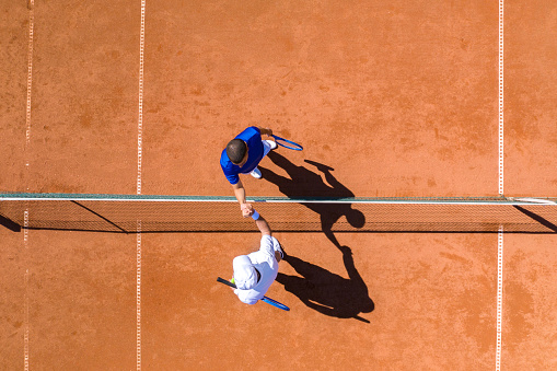 Aerial view of two tennis players greeting each other over the net after finishing the game