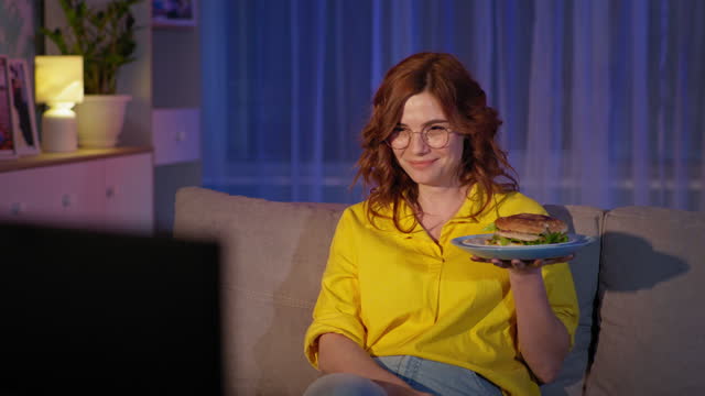 spending time at home, portrait of cheerful girl in glasses laughing from watching funny program on TV, eating fast food at night while sitting on couch in living room, quarantine